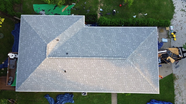 A completed shingle roof seen straight down from above, clean valleys and ridges, a backyard visible below