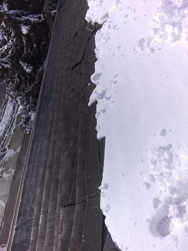 A damaged gutter section being repaired at the roof edge, snow visible in the trees behind