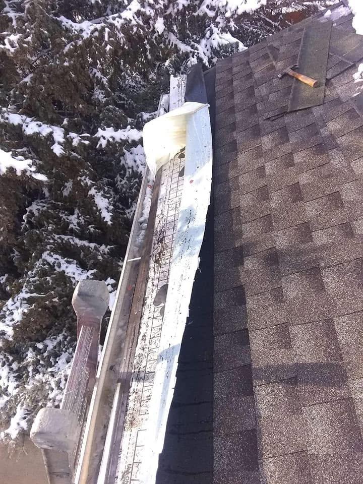 A close view of a roof edge and gutter mid-repair, tools and a hammer visible against shingle and trim