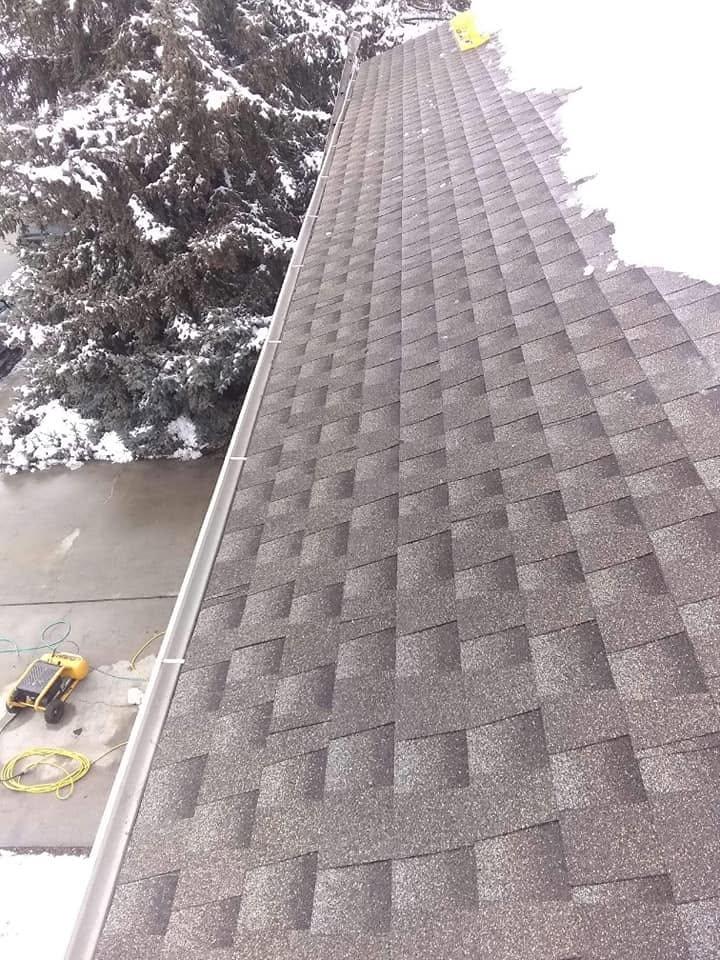 A snow-covered shingle roof with a section cleared, seen from the gutter line looking up toward the ridge