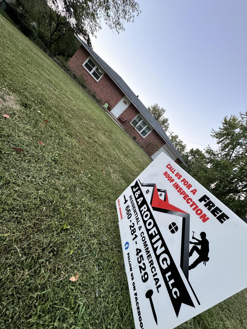 A J & A Roofing yard sign reading Residential and Commercial, Fully Insured, Call us for a free roof inspection, planted on a lawn in front of a brick house